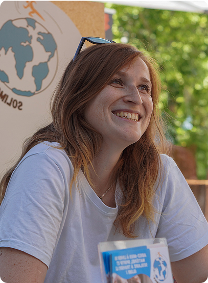 Une étudiante en reconversion se tient souriante dans un cadre naturel, son regard est porté vers la droite, elle s'adresse à quelqu'un hors du cadre tandis qu'elle semble promouvoir l'association Solimouv